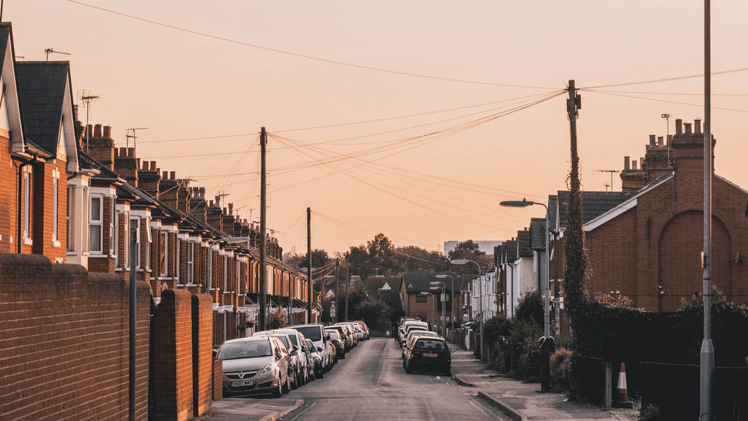 A street of terraced houses, parked cars and telephone wires in Ipswich. The sky is pink.