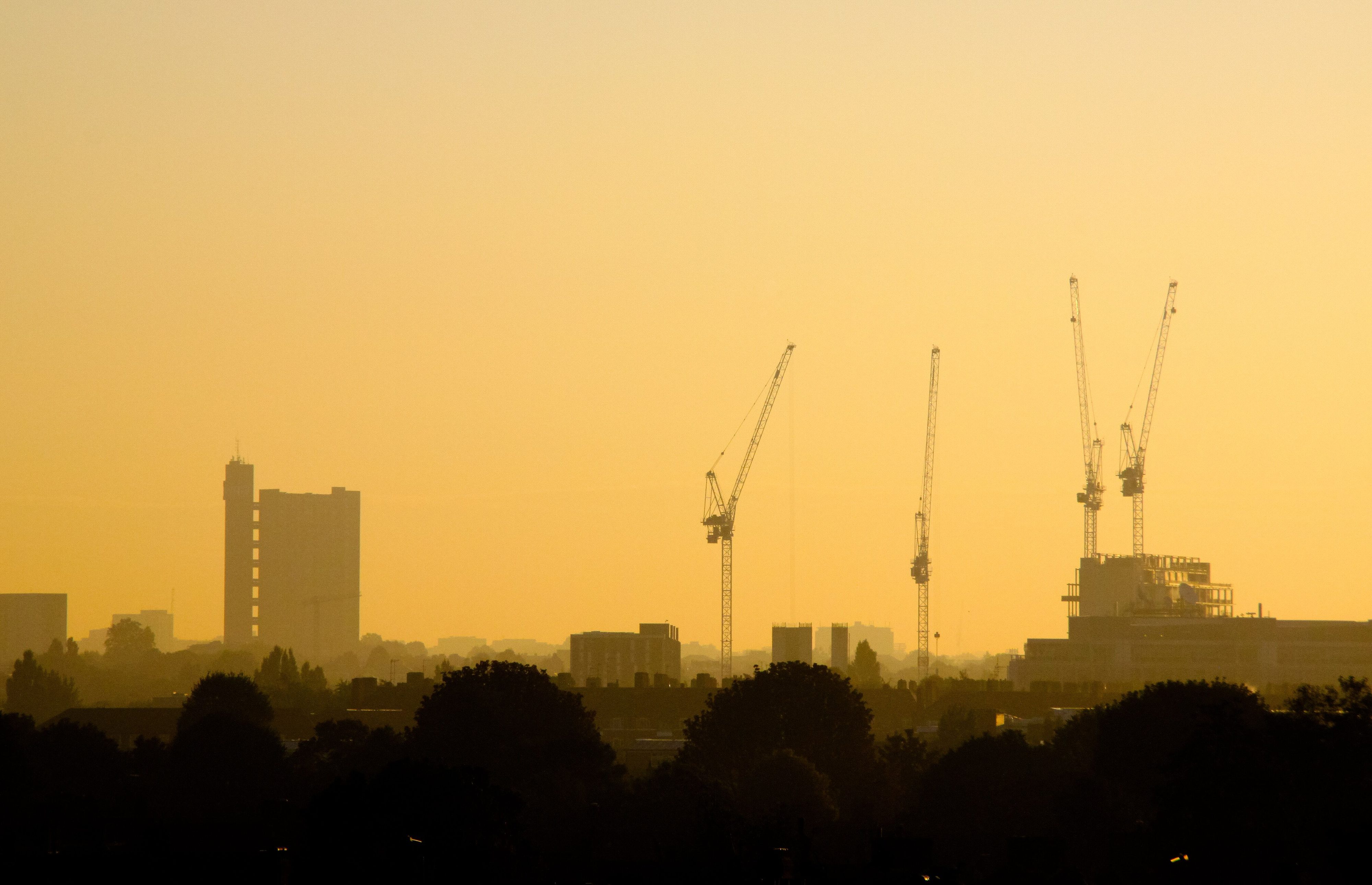 A tower block and cranes on an orange sky