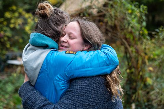 Two people hugging with trees behind.