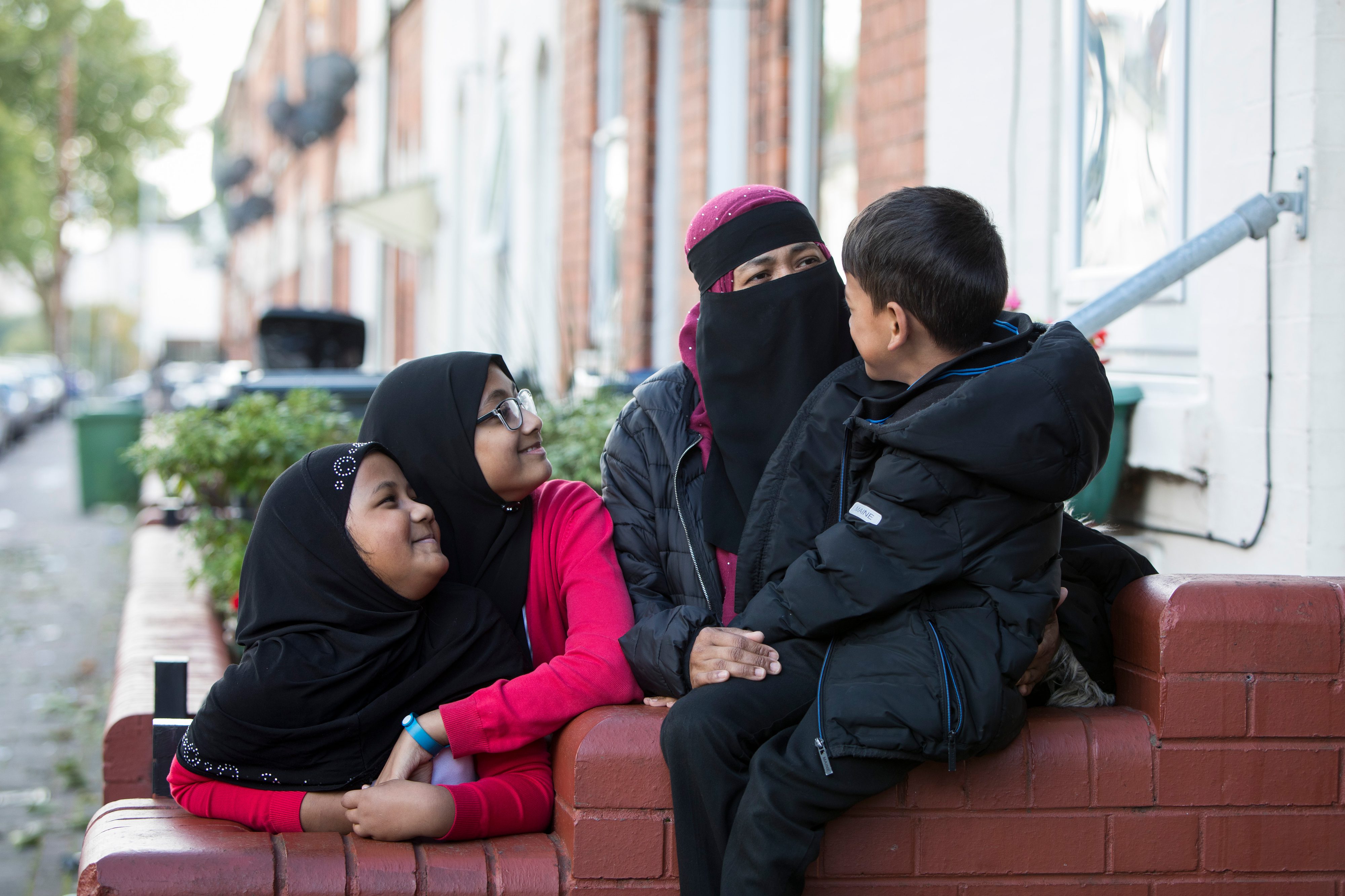 A family stand around a garden wall looking at each other and smiling