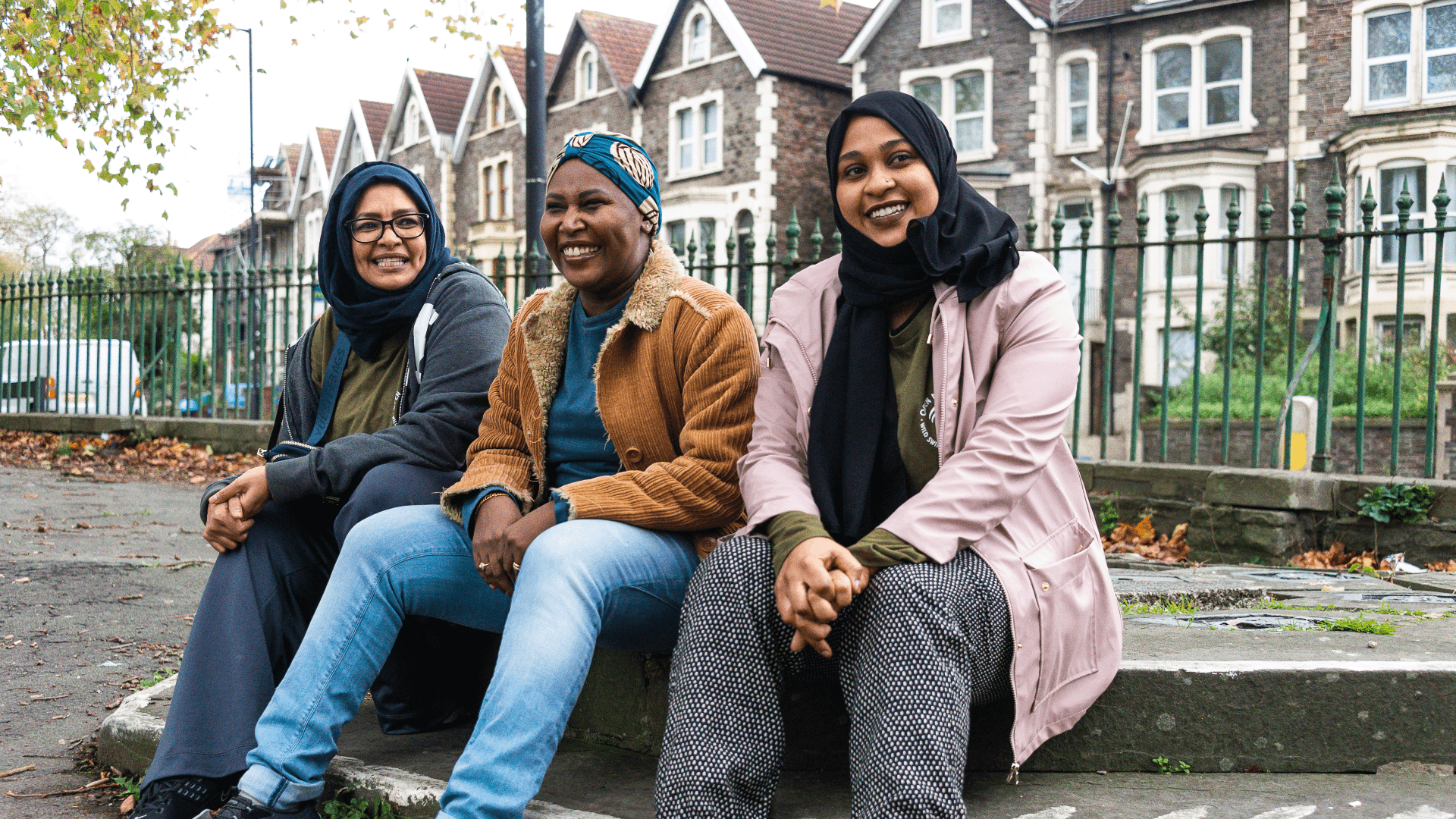 Three women  sit smiling on steps in front of a block of houses.