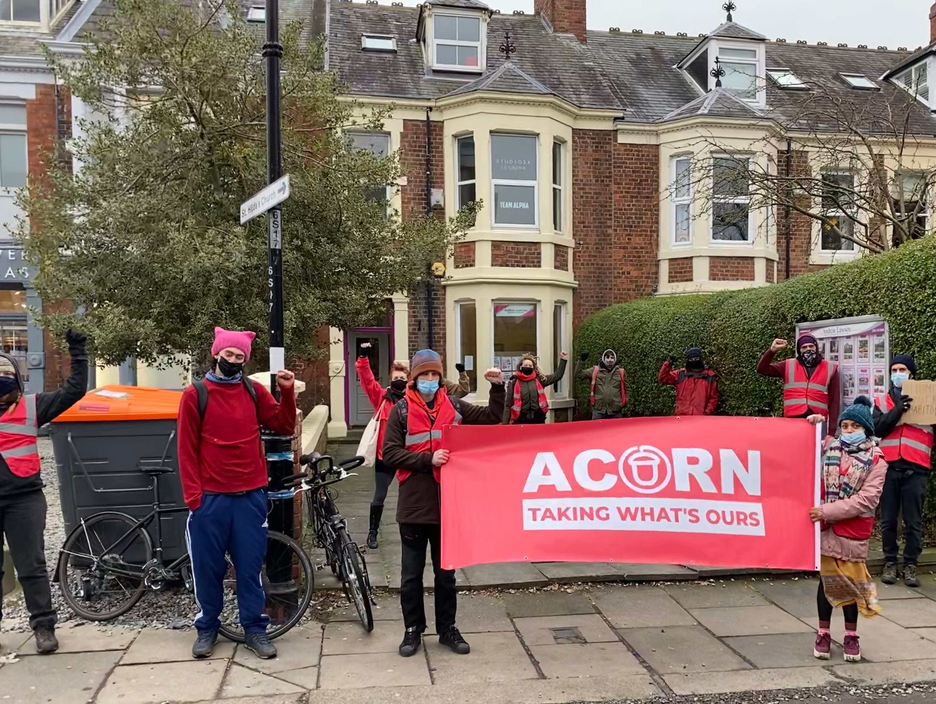 A group of people hold up a banner with ACORN's logo infront of a house