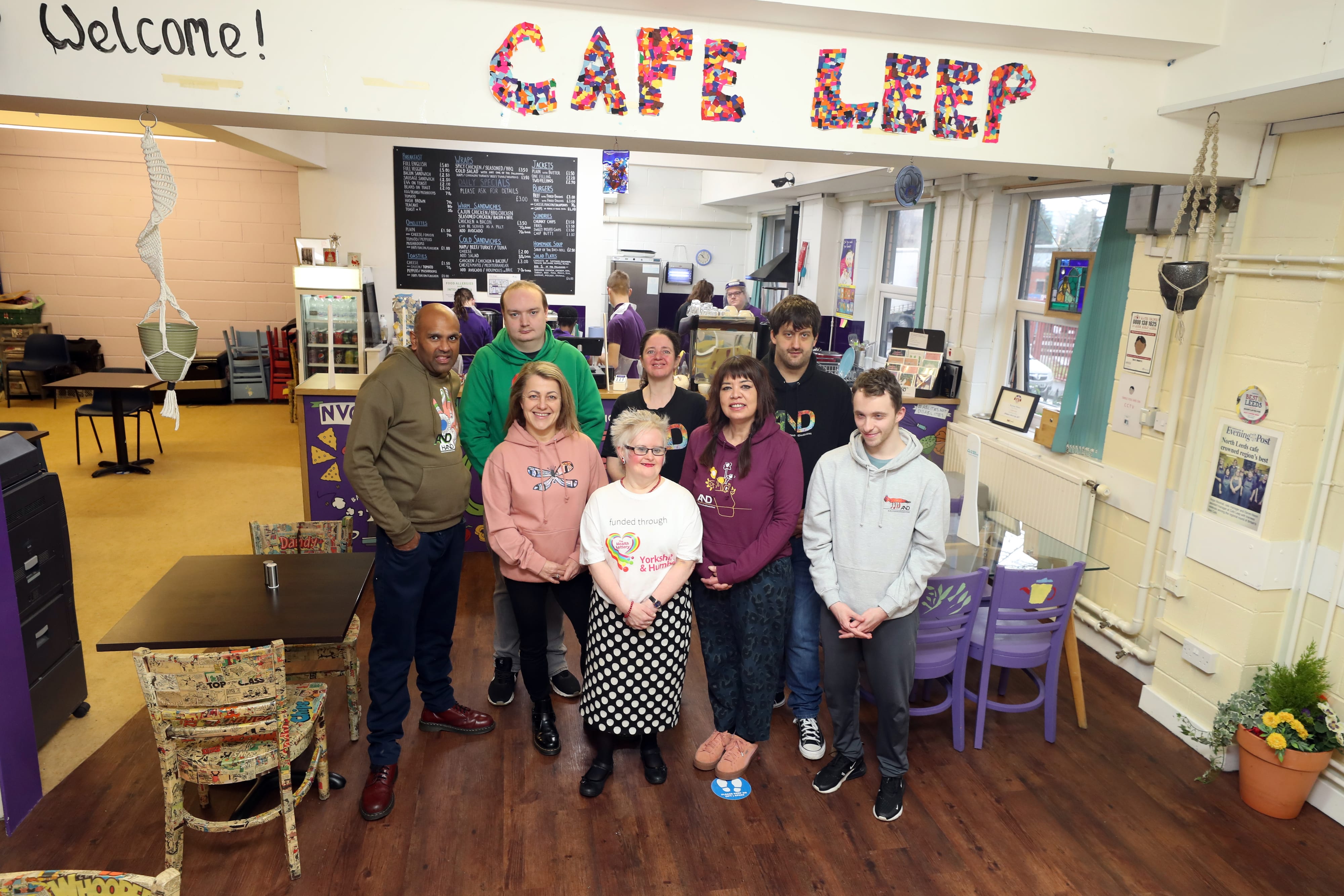 Members from LEEP1 stand under their cafe sign and post for a photo