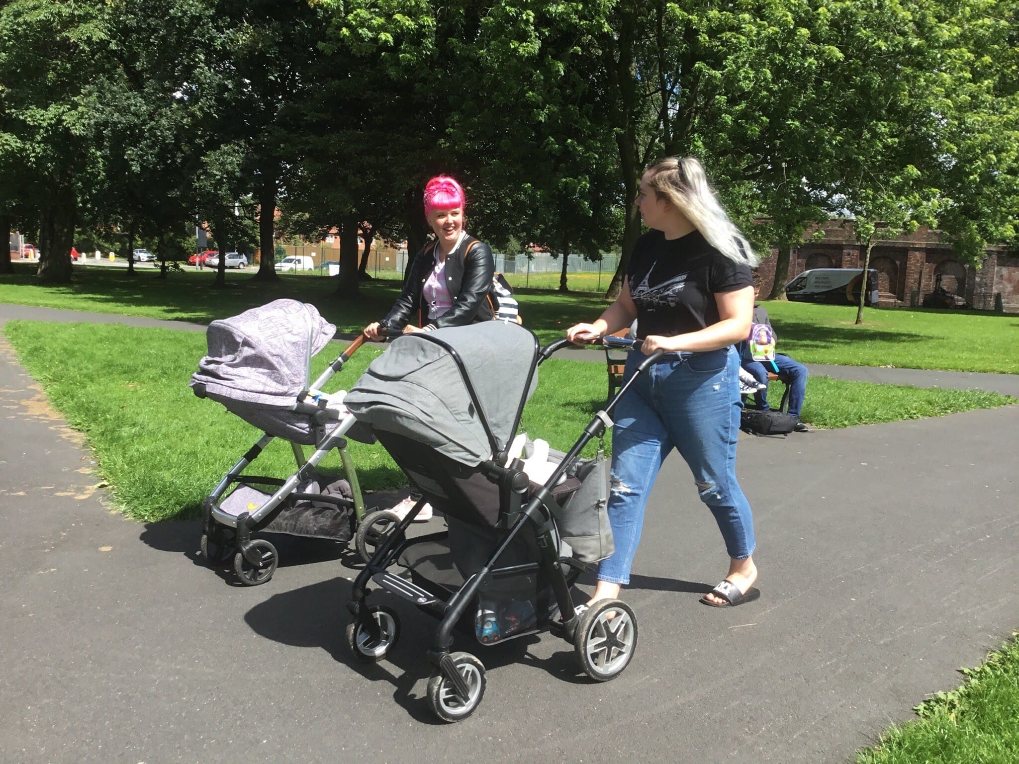 Two people walk with push chairs in a park