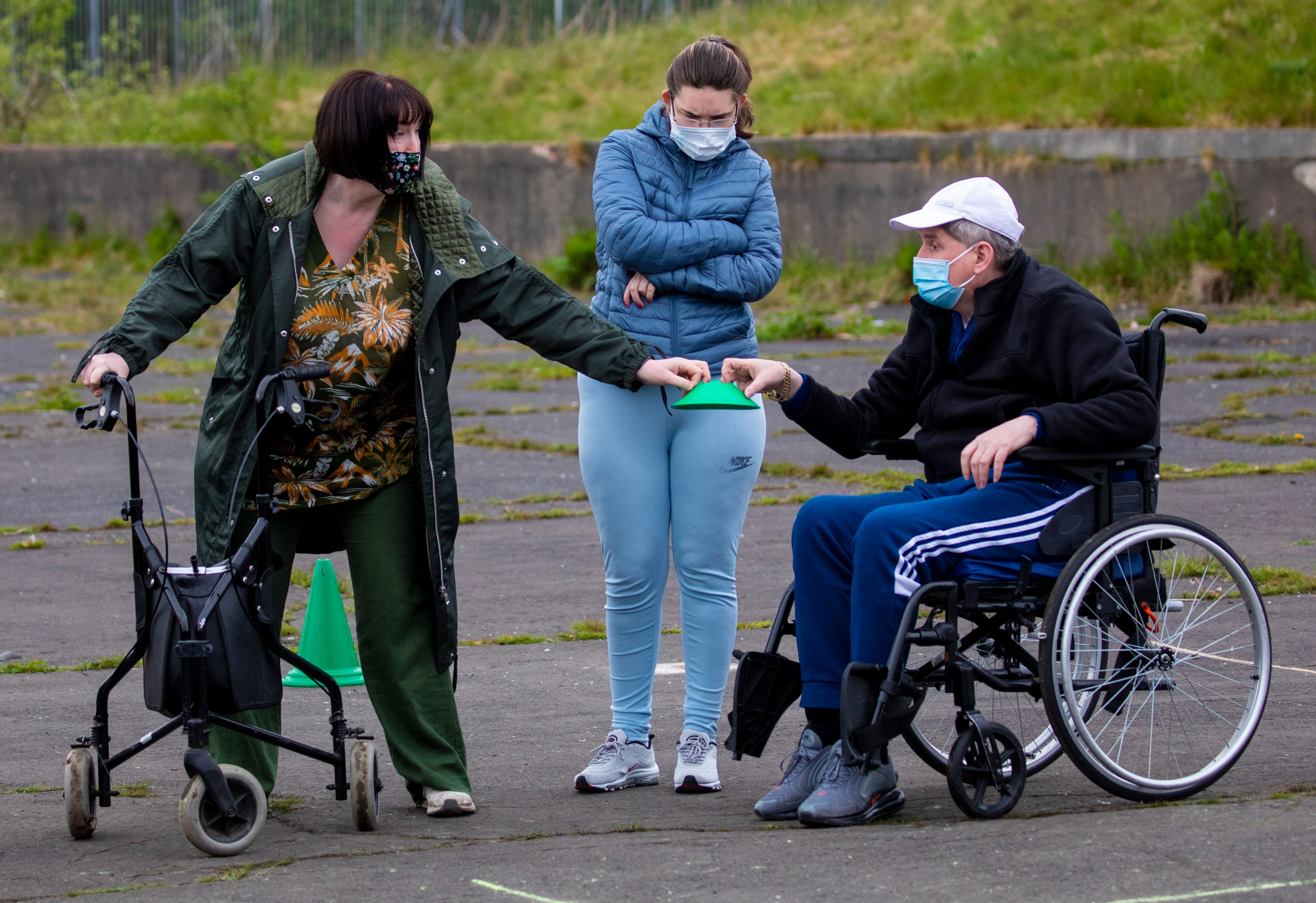 A woman hands a cone to a man in a wheelchair while another woman looks on