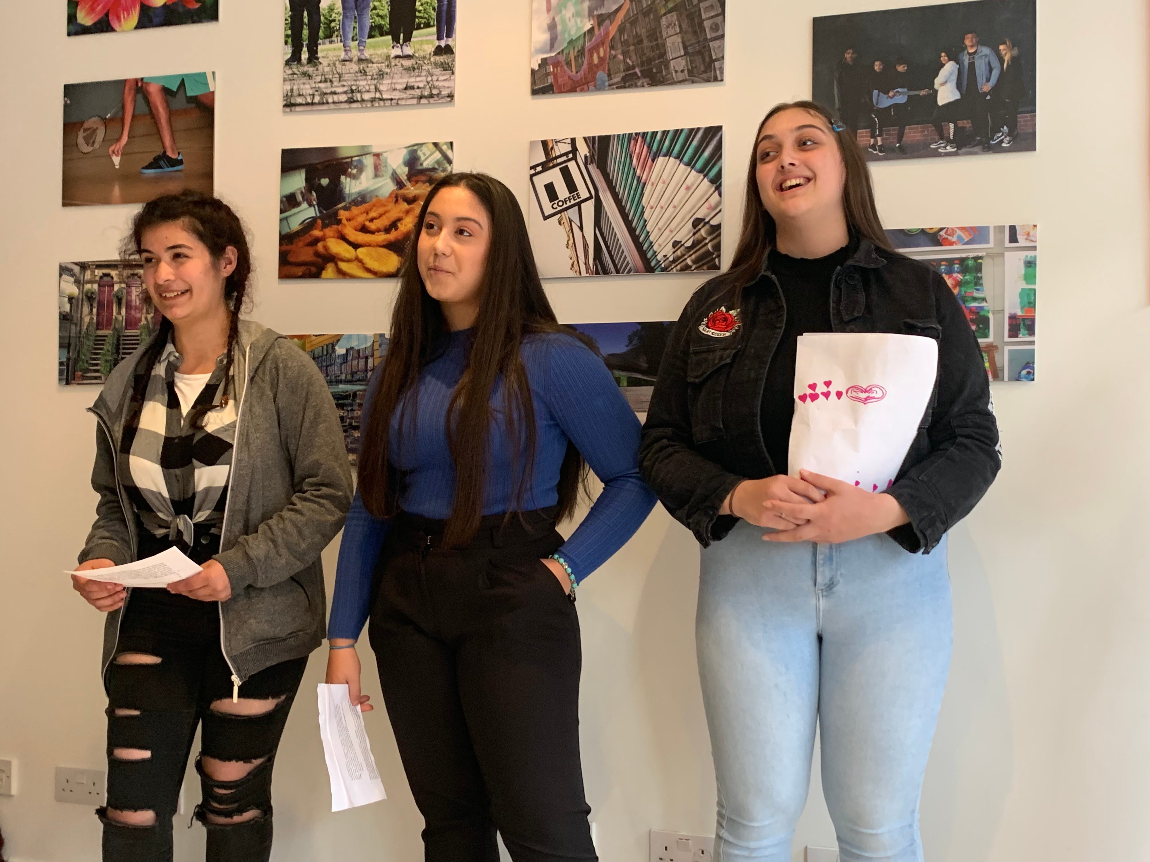 Three young people stand in front of a wall of photography